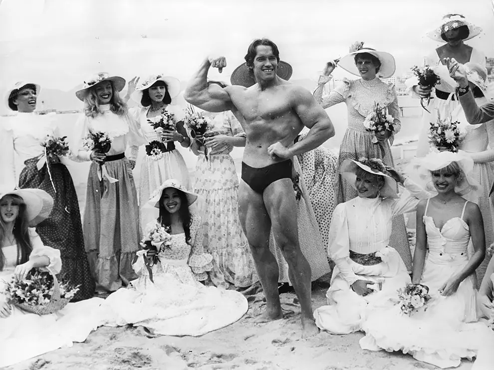 Arnold Schwarzenegger, the film actor who first became famous as Mr. Universe for his magnificent physique, on Cannes beach during the Film Festival with the girls from the Folies Bergere. (Photo by Keystone/Getty Images). 1977